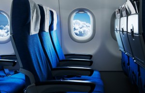 the inside of an airplane with blue seats and a window looking out to the clouds