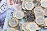 a pile of one pound coins sits on top of a pile of 20 and 5 pound notes